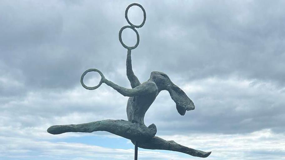 A statue of a hare leaping in the air whilst doing the splits and juggling three things