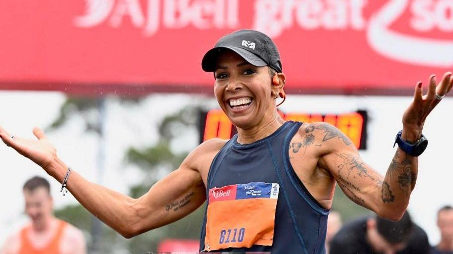 Dame Kelly Holmes at the event smiling and holding her arms up, wearing sports gear.