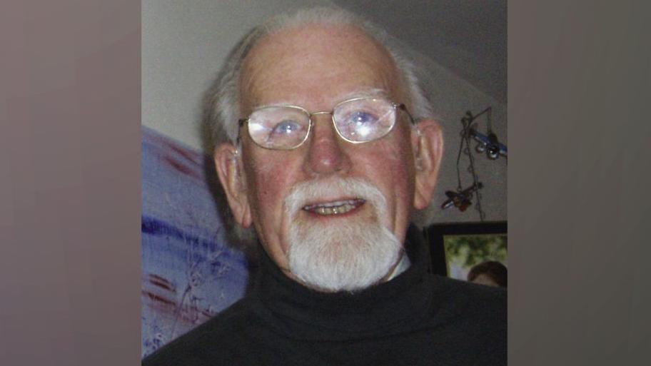 A close-up photograph of George Bramall who has grey hair and and a grey beard. He is wearing silver metal-framed glasses.
