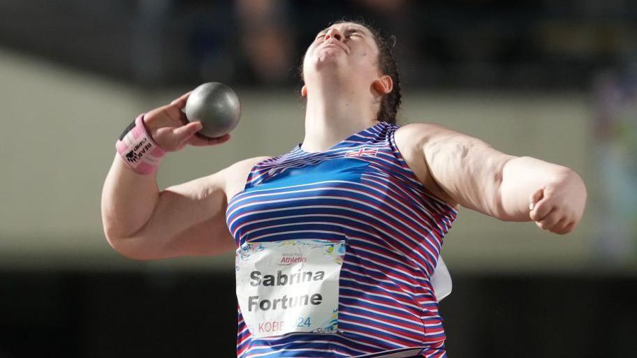 Sabrina Fortune, wearing a striped top, about to throw a shot in Kobe, Japan