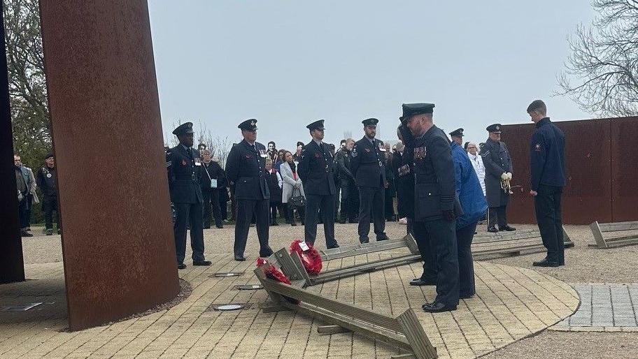 Military personnel stand round the the wreaths that have been placed at the bottom of the memorial.