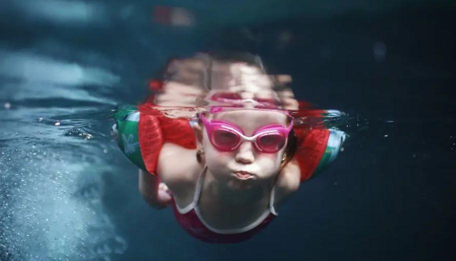 A child wearing goggles and armbands swimming underwater.