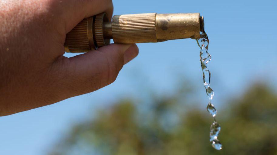 Water dripping from the end of a hosepipe being held up, with a blue sky behind