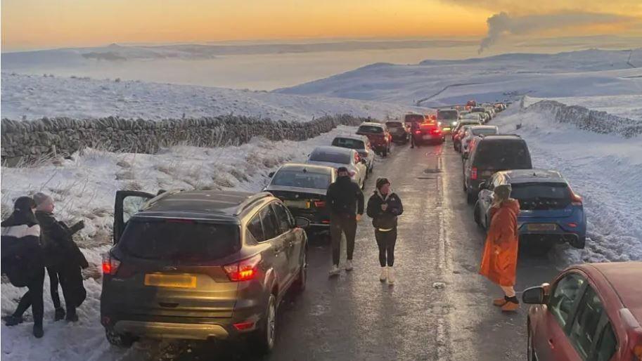 A number of cars across a snowy Peak District Road.
