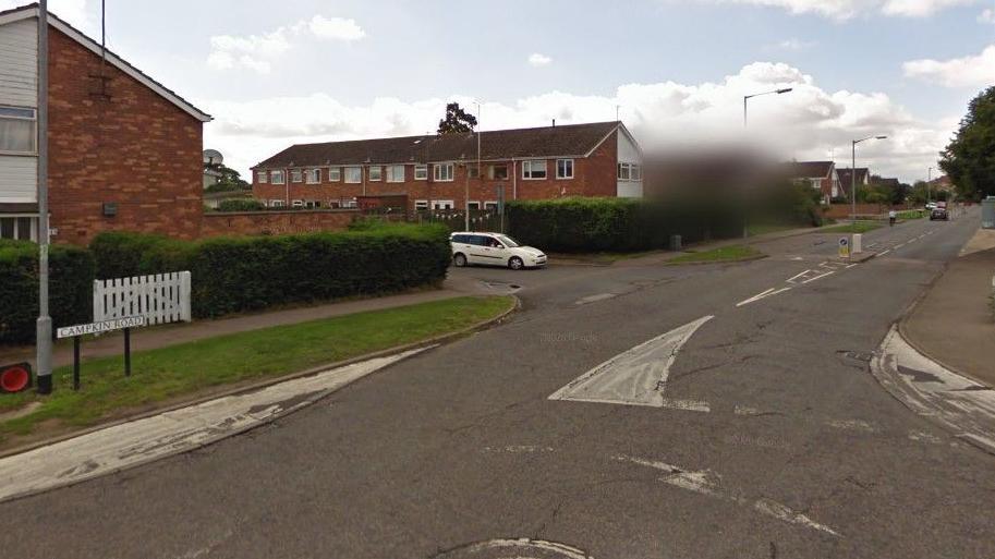 Road with houses along it. A white car can be seen at a junction.