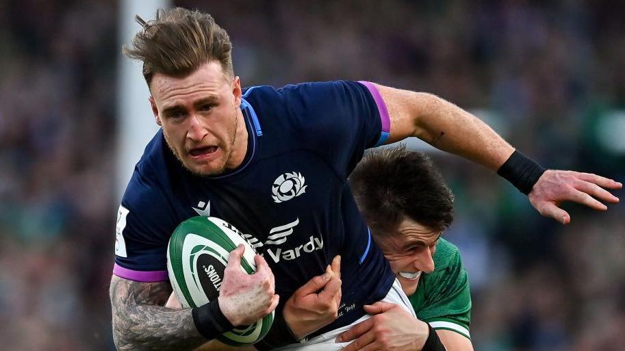 Stuart Hogg - who is wearing a Scotland strip and running with a rugby ball - being tackled by an opponent