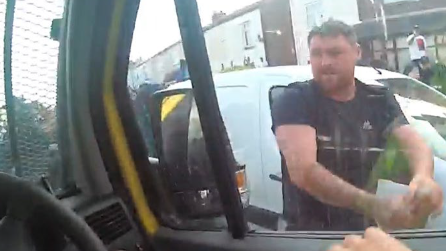 Luke Moran is seen outside the police vehicle after making an attempt to pull off the wing mirror. You can tell there is an officer in the driver's seat as a hand is visible resting on the inside of the window