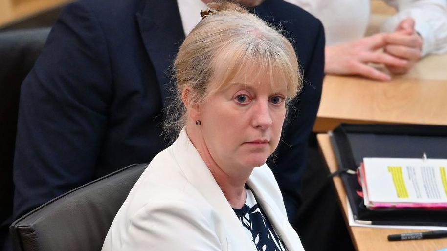 Shona Robison, Scotland's finance secretary, She has blonde hair which is tied up and is wearing a white blazer.