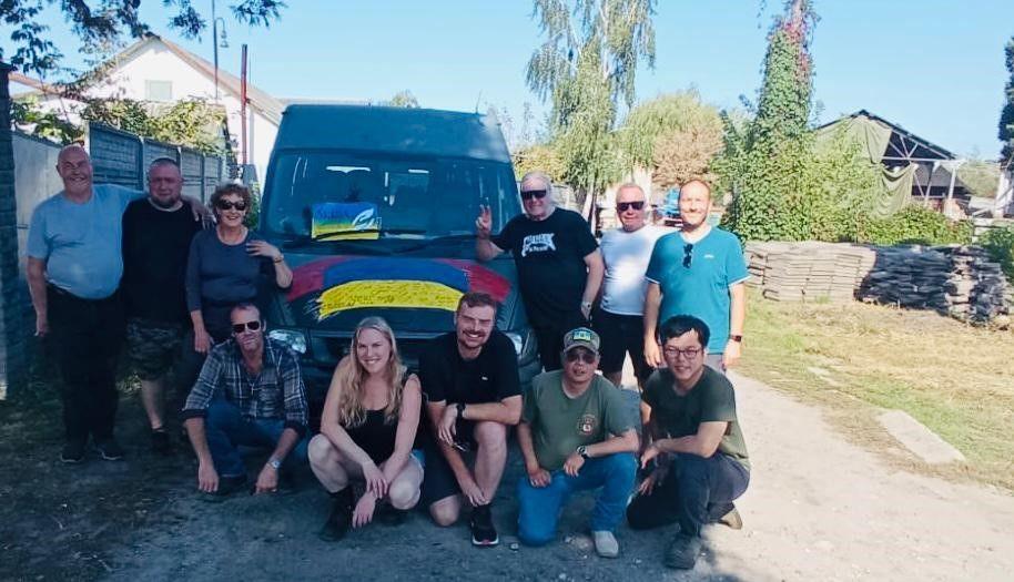 A group of volunteers pose in front of a minibus parked in a Ukrainian village.