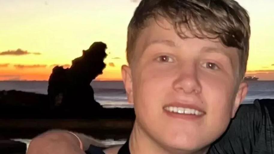 Matthew Daulby smiling in front of a beach as the sun is setting 