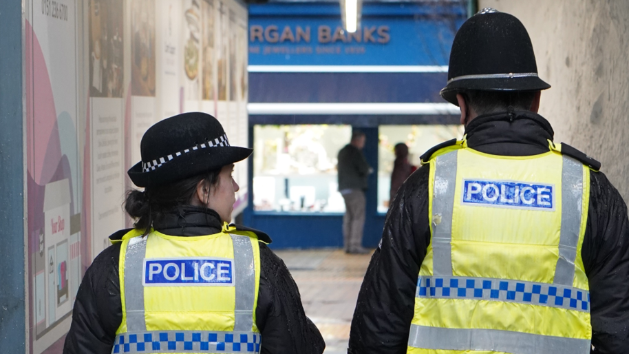 Two police officers walk down a corridor 