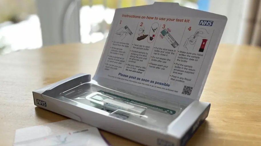 A close-up of a home-testing kit, consisting of a small white cardboard box containing a stick and a container in packaging, laid open on a dining room table