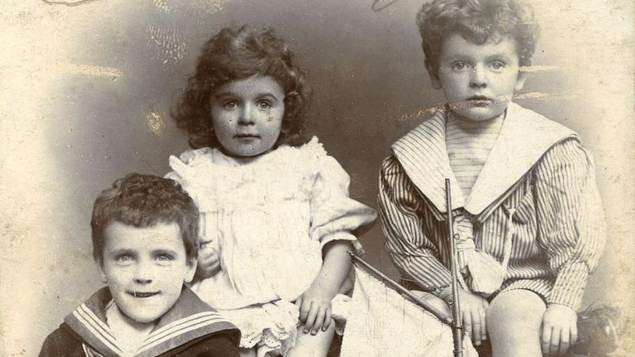 A Victorian, sepia photograph showing three young children wearing fashions from the era, including sailor suits.