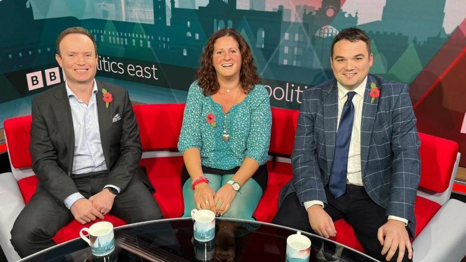 Conservative councillor Richard Rout (l-r), Labour councillor Elisa Meschini and Reform UK councillor Robin Hunter-Clarke discussed car parking on BBC Politics East. The picture was taken in the studio. The three politicians are sitting next to each other on a red sofa.