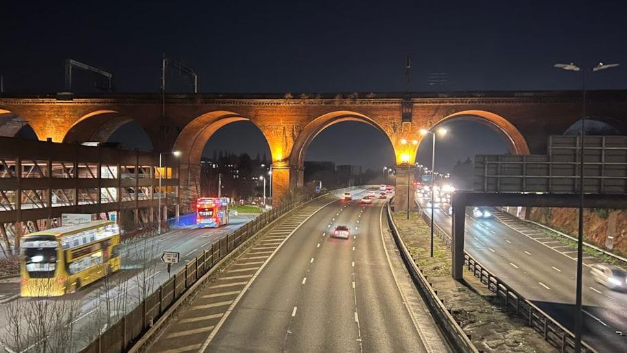 Evening view of Stockport Viaduct which crosses over the M60 motorway showing two buses on a road by the motorway