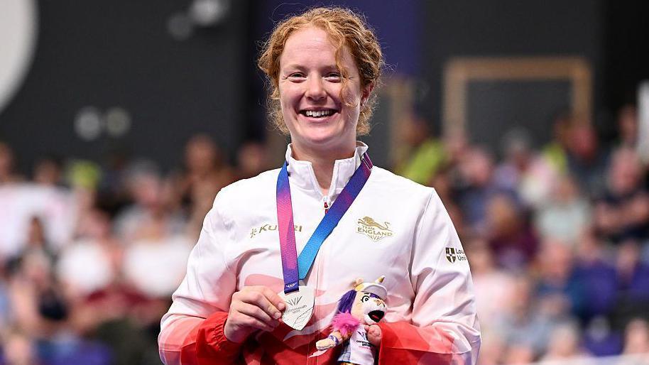 Morgan Newberry stands on the podium with her silver medal in her hand and holding a small mascot toy.
