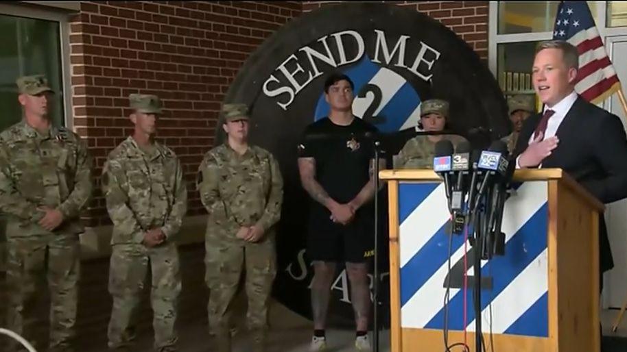 A screenshot of a press conference held by the US army on Thursday. In it, US Army Secretary Dan Driscoll is seen speaking at a wooden podium, with several microphones in front of him. Six soldiers are seen standing on his left, with five of them in full Army uniform and one wearing black shorts and a T-shirt. A US flag on a pole is also seen behind him.