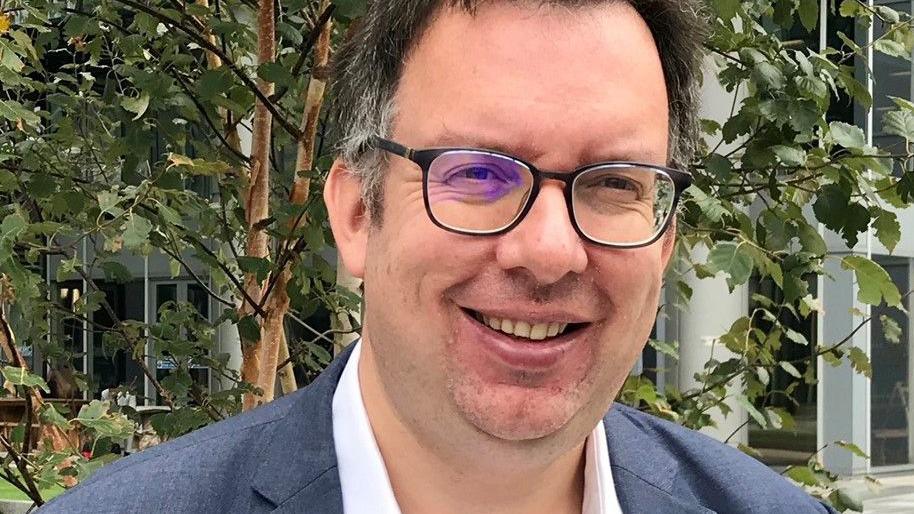 Richard Blakeway pictured in a blue jacket and white shirt. He is wearing glasses and smiling at the camera. 