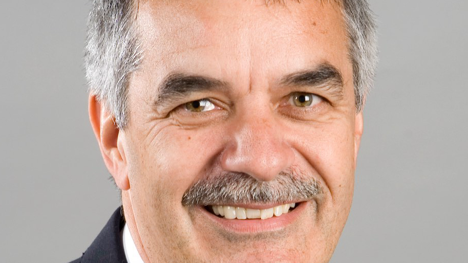 Mike Jessop smiling for the camera in a close up headshot. He has a greying moustache and you can see the sides of his hair. He has light brown eyes.