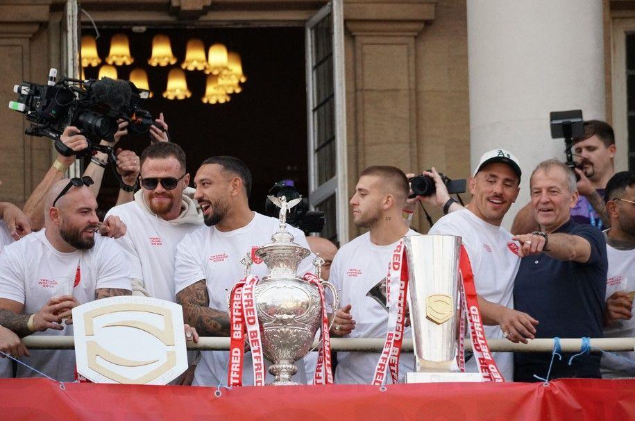 Hull KR players, wearing white shirts are standing on the balcony of Hull City Hall with three trophies in front of them