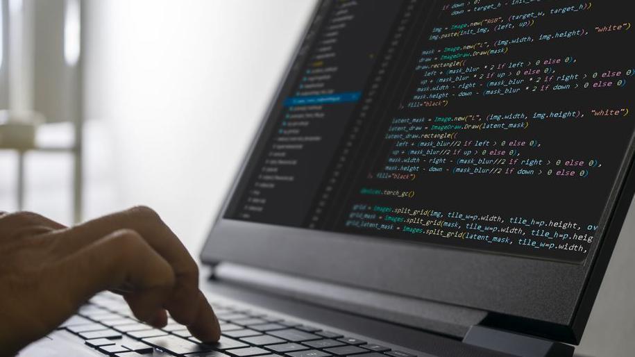 Generic image of am open laptop computer. The screen depicts code. To the left of the image fingers tapping the keyboard can be seen.