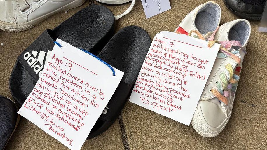 Two pairs of shoes, one a pair of black flip flops, the other a pair of red and white plimsols. They have white cards attached detailing children's journeys through the Send system in red writing. One pair belongs to a child aged nine, the other to a child aged seven.