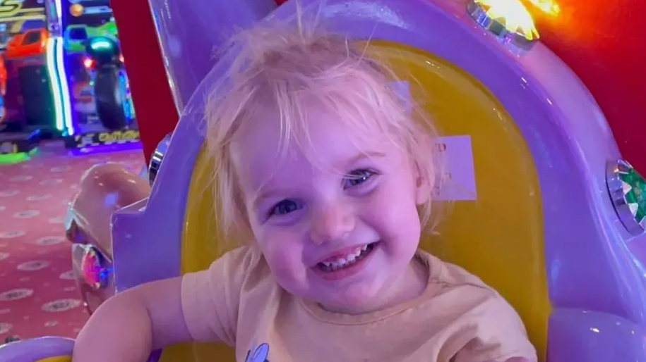 Little girl smiling at the camera, sitting in a brightly coloured chair at an amusement arcade