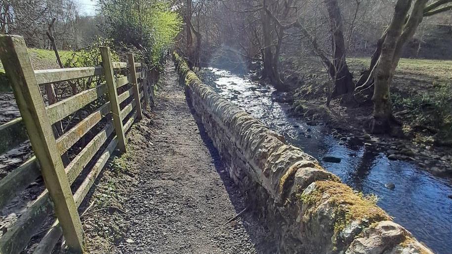 A path runs beside a wall adjacent to a river