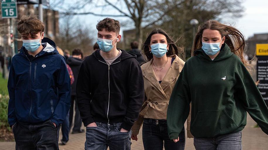 Pedwar myfyriwr mewn mygydau yn cerdded ar gampws Prifysgol Caint yn dilyn nifer o achosion o lid yr ymennydd yn lleol