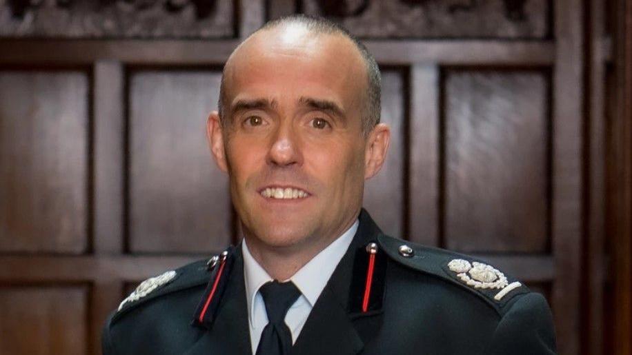 Rob Barber, chief fire officer for Staffordshire Fire and Rescue Service, is stood against a wood-panelled wall in his uniform.