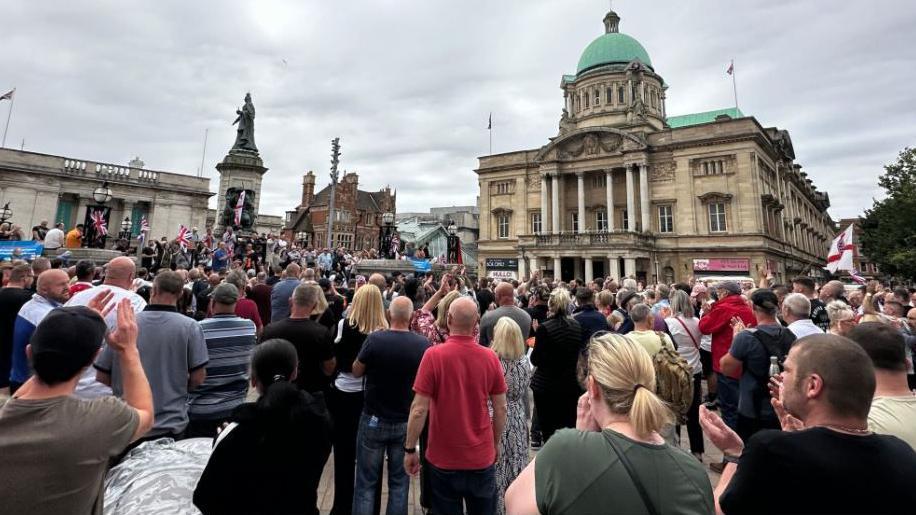 Hundreds of people standing in Queen Victoria Square, Hull, with some holding Cross of St George and Union flags.