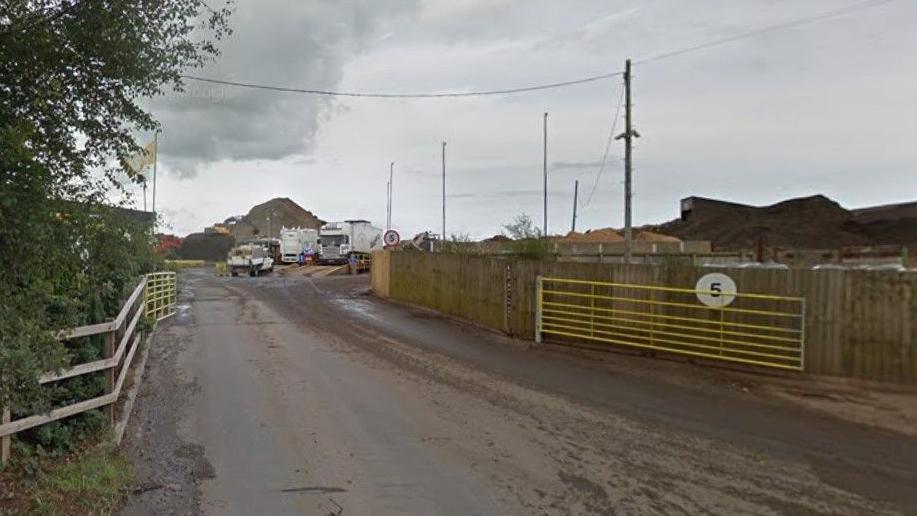 Gates to the Eco recycling and waste processing plant. Beyond the entrance are some lorries and large mounds of what appears to be soil.