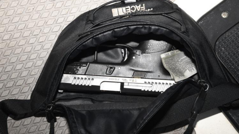 A black North Face bum bag sits on a metal table. It is open and a black handgun is stored inside.