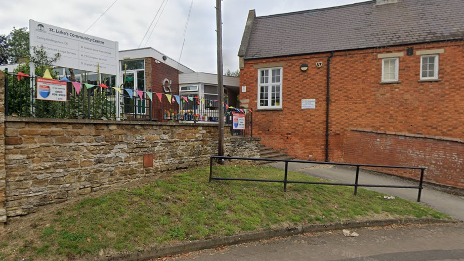 A red brick building with a black iron fence and multi coloured bunting draped over the fence. 