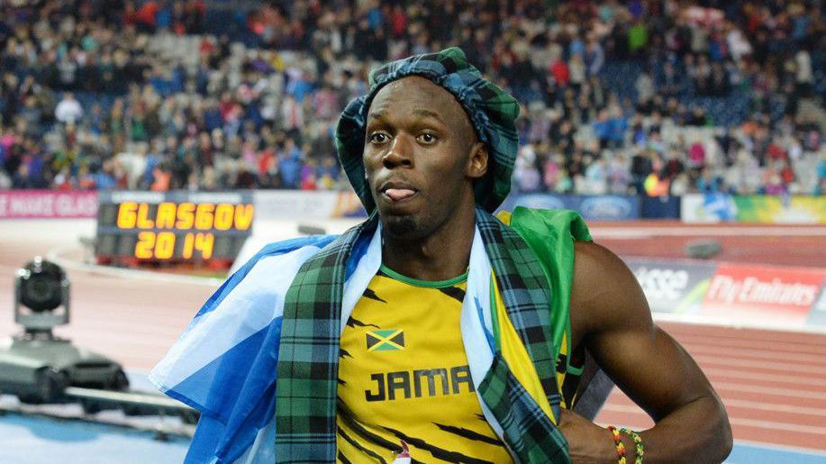 Usain Bolt celebrating at the Commonwealth Games, with a Scotland flag over his shoulders and a bunnet on his head