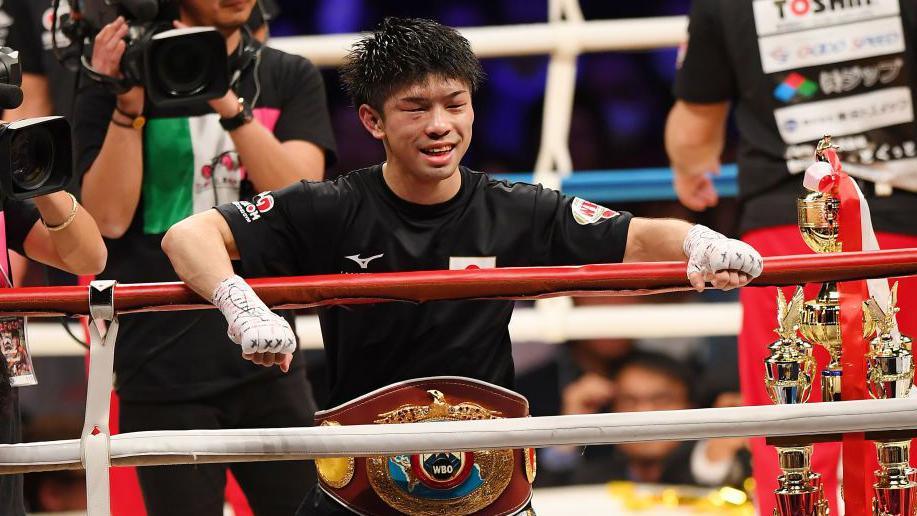 Kosei Tanaka smiles with his arms over the ropes and his WBO title around his waist