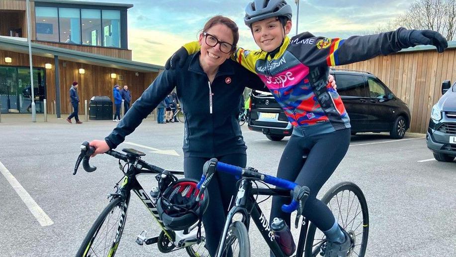 A woman on a bike with her arm around a boy who is also on a bike.