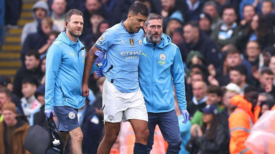 Manchester City midfielder Rodri being helped off the pitch by physios