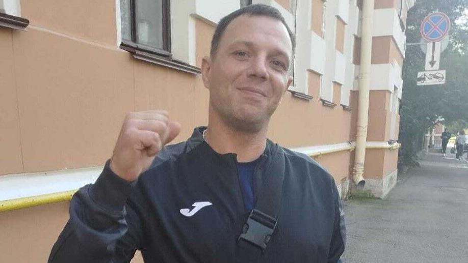 A man in a tracksuit pumps the air with one hand while the other, wearing a gold watch, holds a white carrier bag