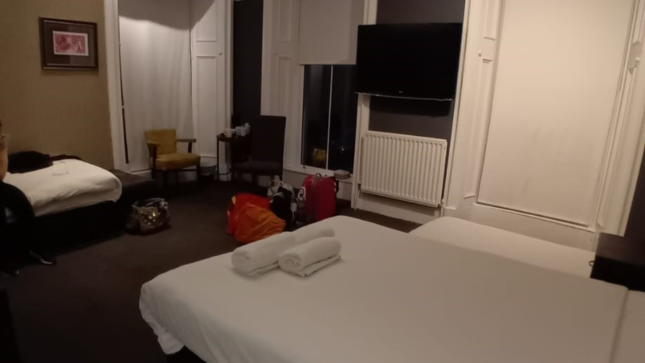 two single beds in a hotel room which has some bags and suitcases on the floor