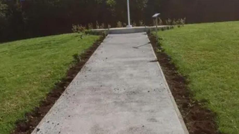 A concrete path with upturned soil in a row along each side - holes can be seen when plants would once have been.