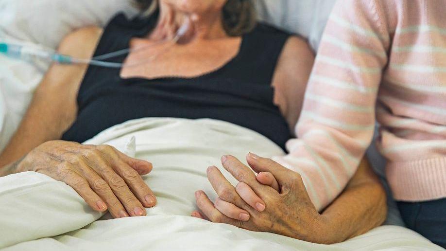 Patient in a hospital bed holding hands with a loved one who is visiting.