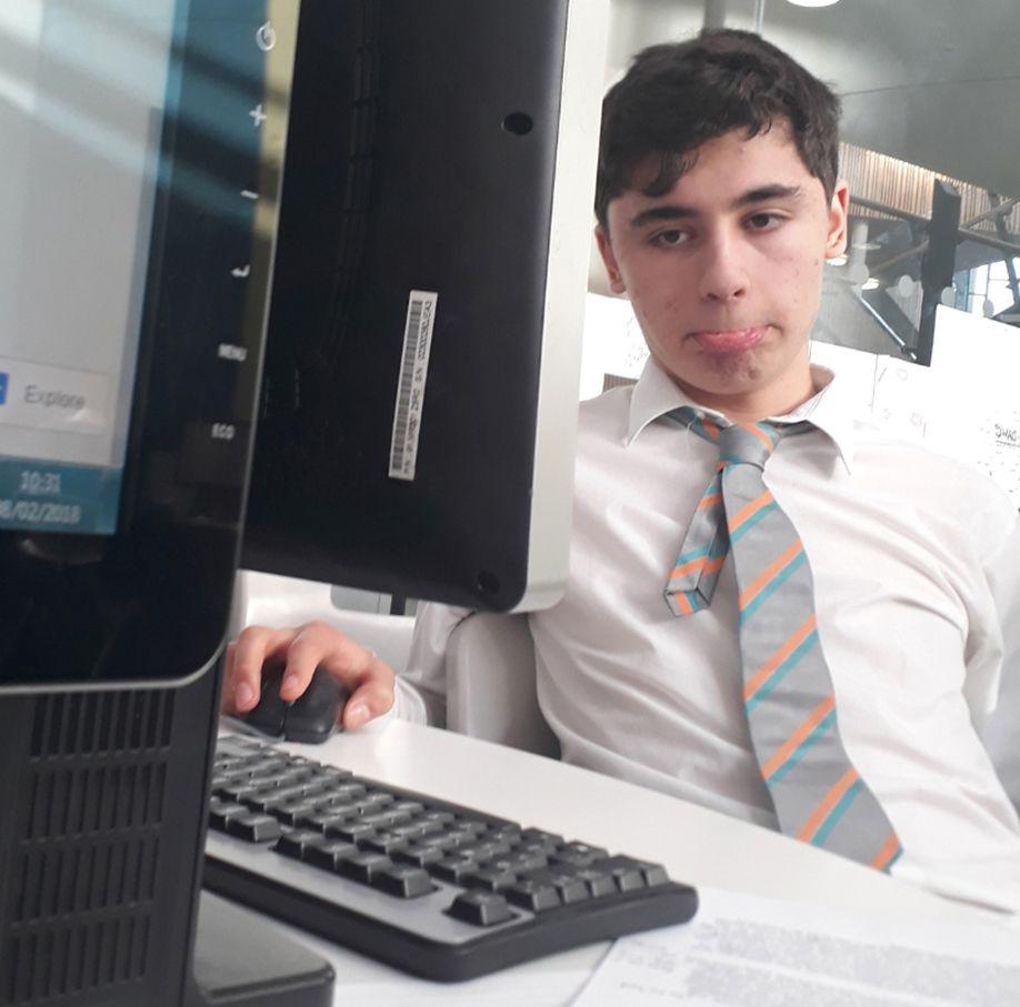 Daniel Khalife is pictured at school wearing a shirt and striped tie with top button undone, while using a computer in a classroom.