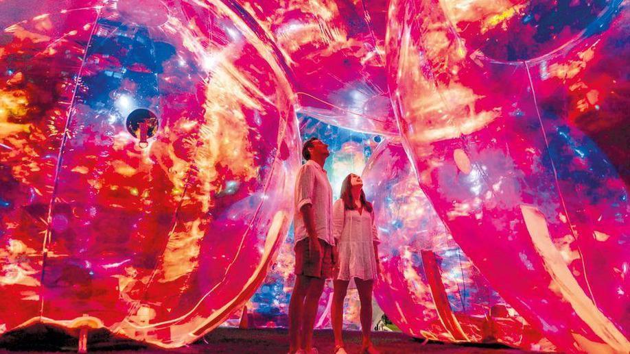 One of the installations at a previous Leeds Light Night festival. Two people stare up at glowing red and yellow spheres surrounding them. 