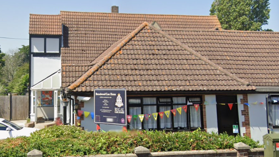 The white care home building, which has colourful bunting draped across the front. It has windows with brown frames.