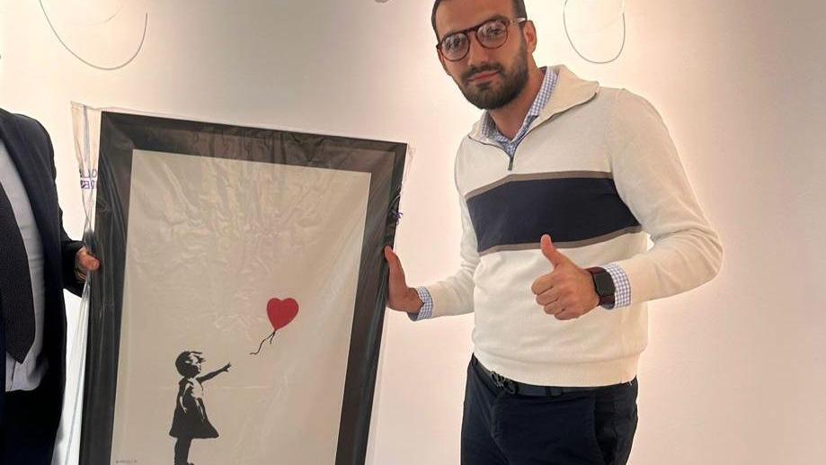 Lindor Mehmetaj holding the recovered artwork giving a thumb up to the camera
