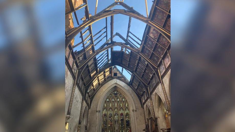 The chapel with a stained glass window. The roof is fire damaged with large holes in it.