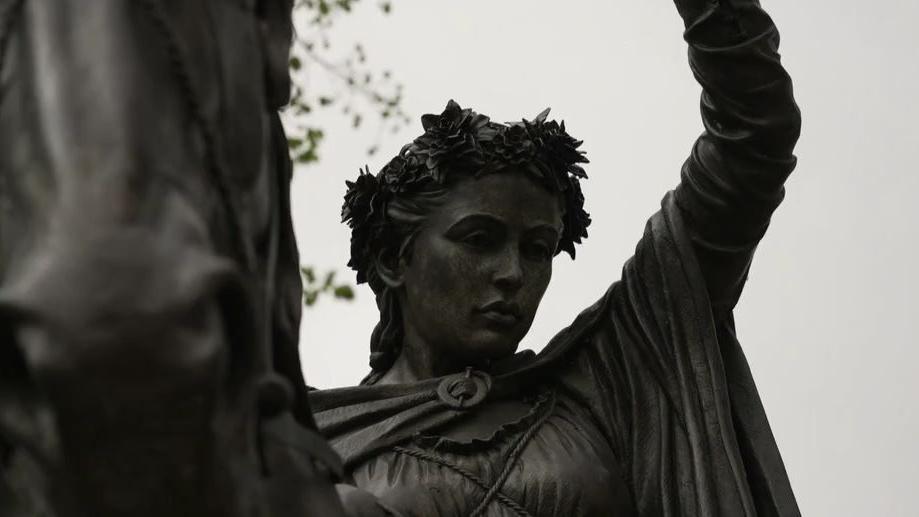 A close up of the lady's face against a grey sky. The horse is also on the shot.