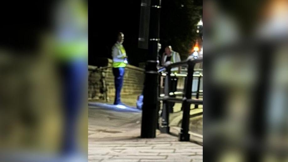 Two people with hi-vis jackets looking at a silver suitcase