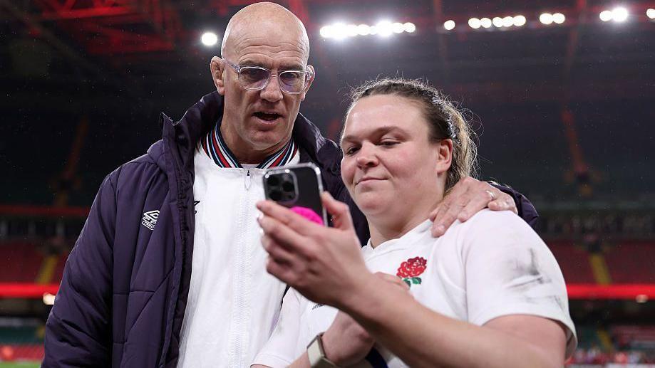 Sarah Bern shows John Mitchell her phone